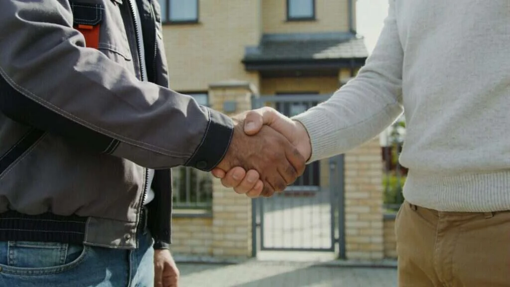 Poignée de main entre un installateur et son client devant la maison